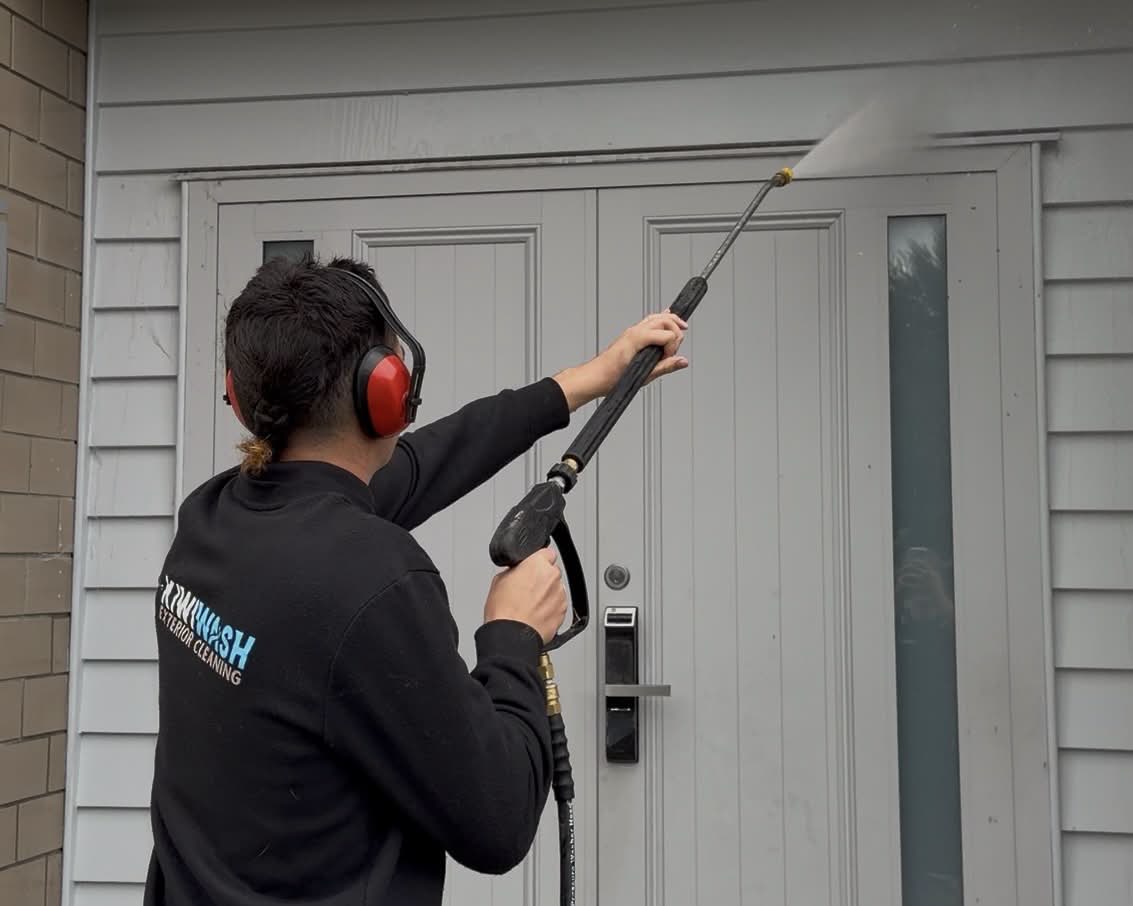 Kiwi Wash team member soft washing a weatherboard entryway